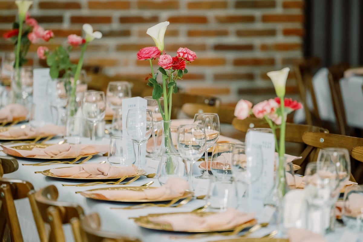 Elegant wedding reception tables decorated with minimalist floral centerpieces featuring vibrant ranunculus, gerbera daisies and graceful calla lilies