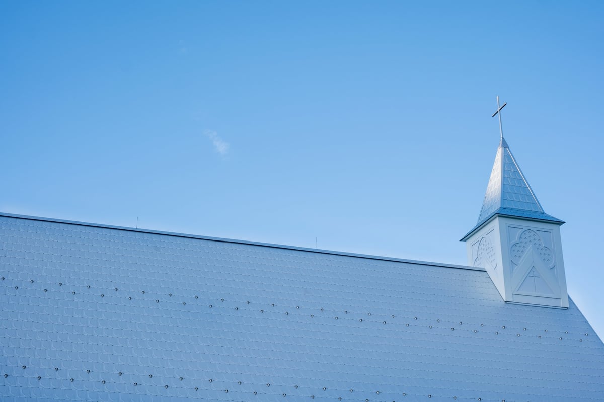 A low angle shot showing a white church roofline and a small steeple topped with a christian cross under a bright open sky