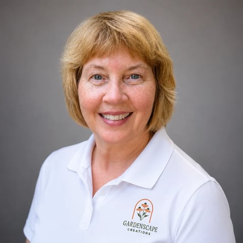 Professional headshot of a smiling woman with shoulder-length blonde hair wearing a white polo shirt with a Gardenscape Creations logo